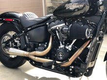Load image into Gallery viewer, A black motorcycle with the focus on the exhaust system, which is silver in color. The motorcycle is parked against a plain wall backdrop.
