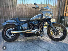 Load image into Gallery viewer, A black motorcycle with the focus on the exhaust system, which is silver in color. The motorcycle is parked against a plain wall backdrop.