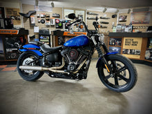 Load image into Gallery viewer, A black motorcycle with the focus on the exhaust system, which is silver in color. The motorcycle is parked against a plain wall backdrop.